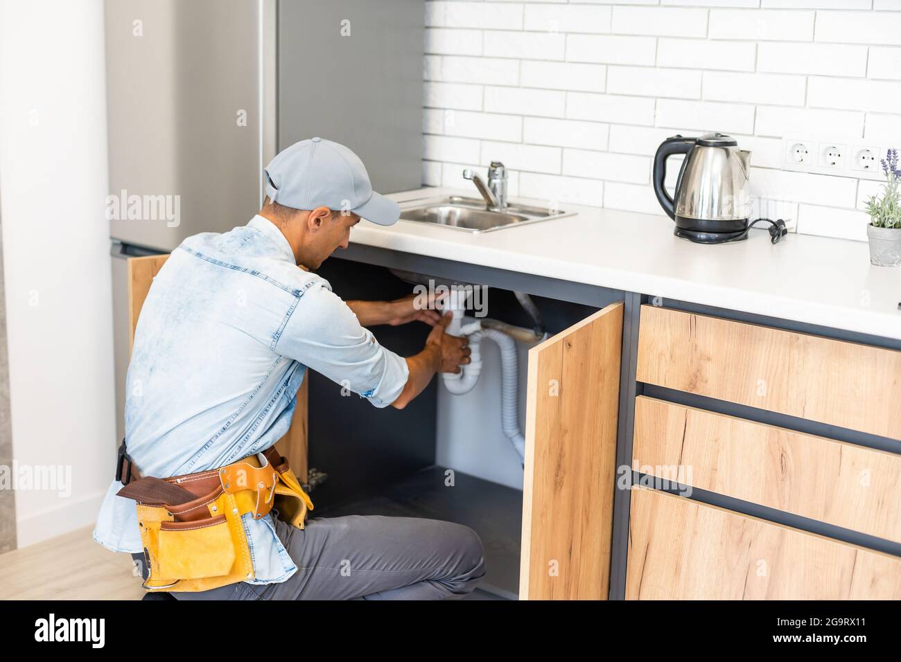 plumber fixes sink siphon by two pipe-wrenches in kitchen. Stock Photo