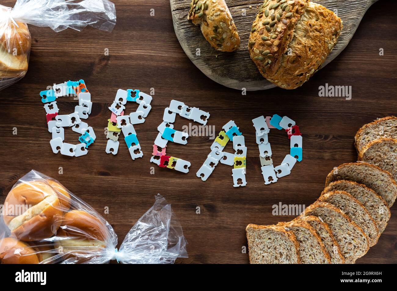 Top down view of the word bread made from the bread bag packaging clips, surrounded by various types of bread. Stock Photo