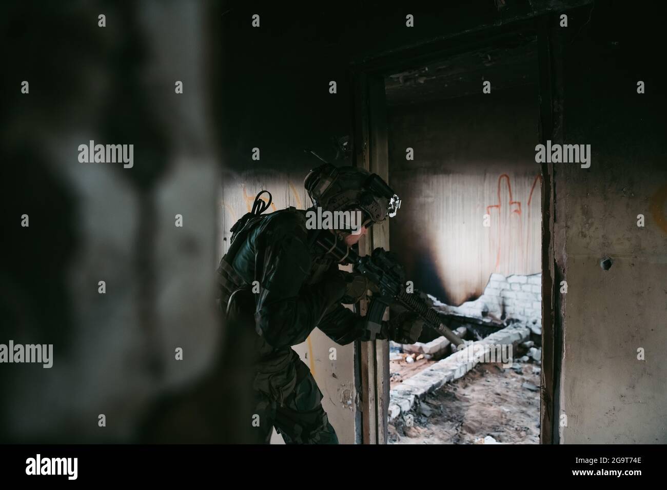 Military man with assault rifle standing inside building, he is ready ...