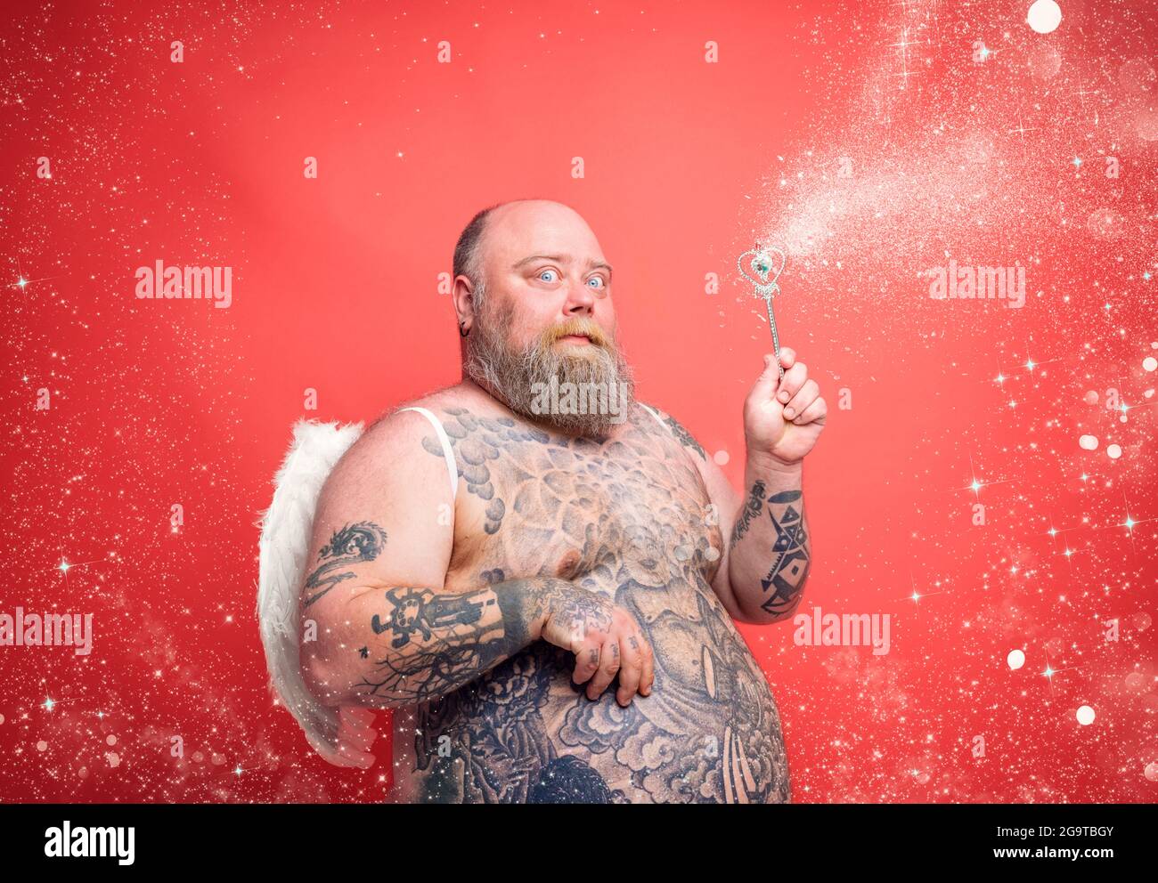 Fat thoughtful man with beard ,tattoos and wings acts like an magic fairy Stock Photo