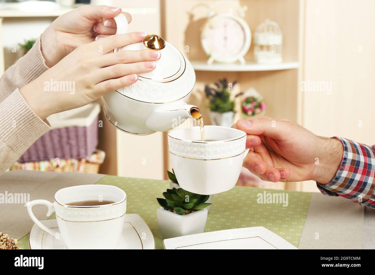 Female and male hands with cups of tea, close-up, on home interior ...