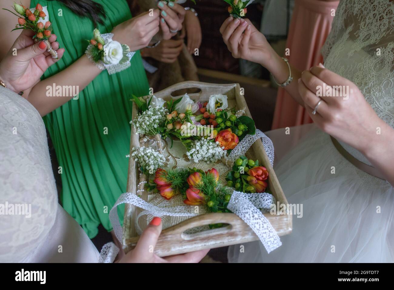 Bride and bridesmaids or female friends around a vintage wooden tray selecting freesias and berries boutonnieres to be used as accessories Stock Photo