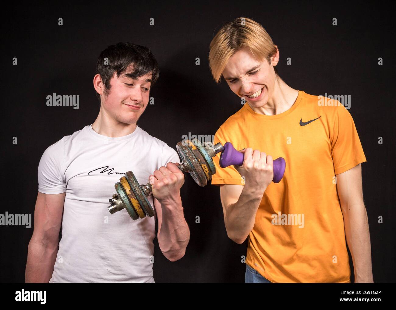 Two male youths doing dumbbell curls, one strong, one weak Stock Photo