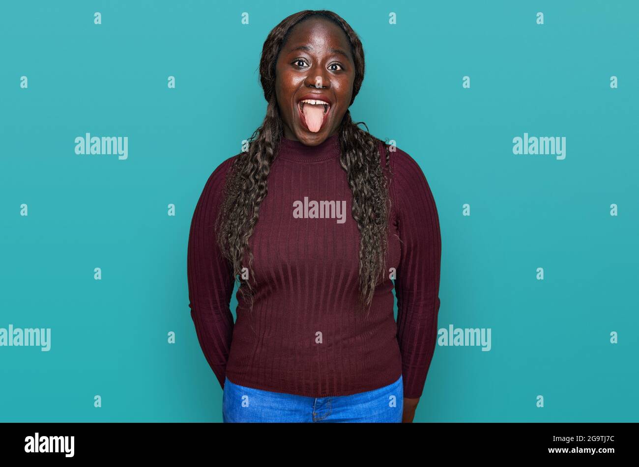 Young african woman wearing casual winter sweater sticking tongue out ...