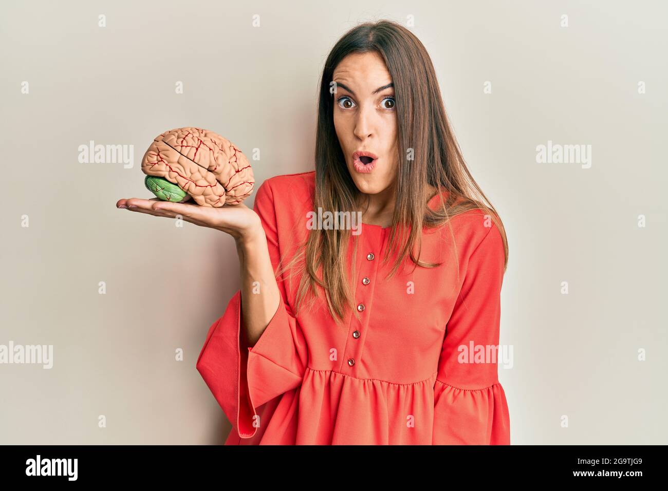 Young beautiful woman holding brain scared and amazed with open mouth ...