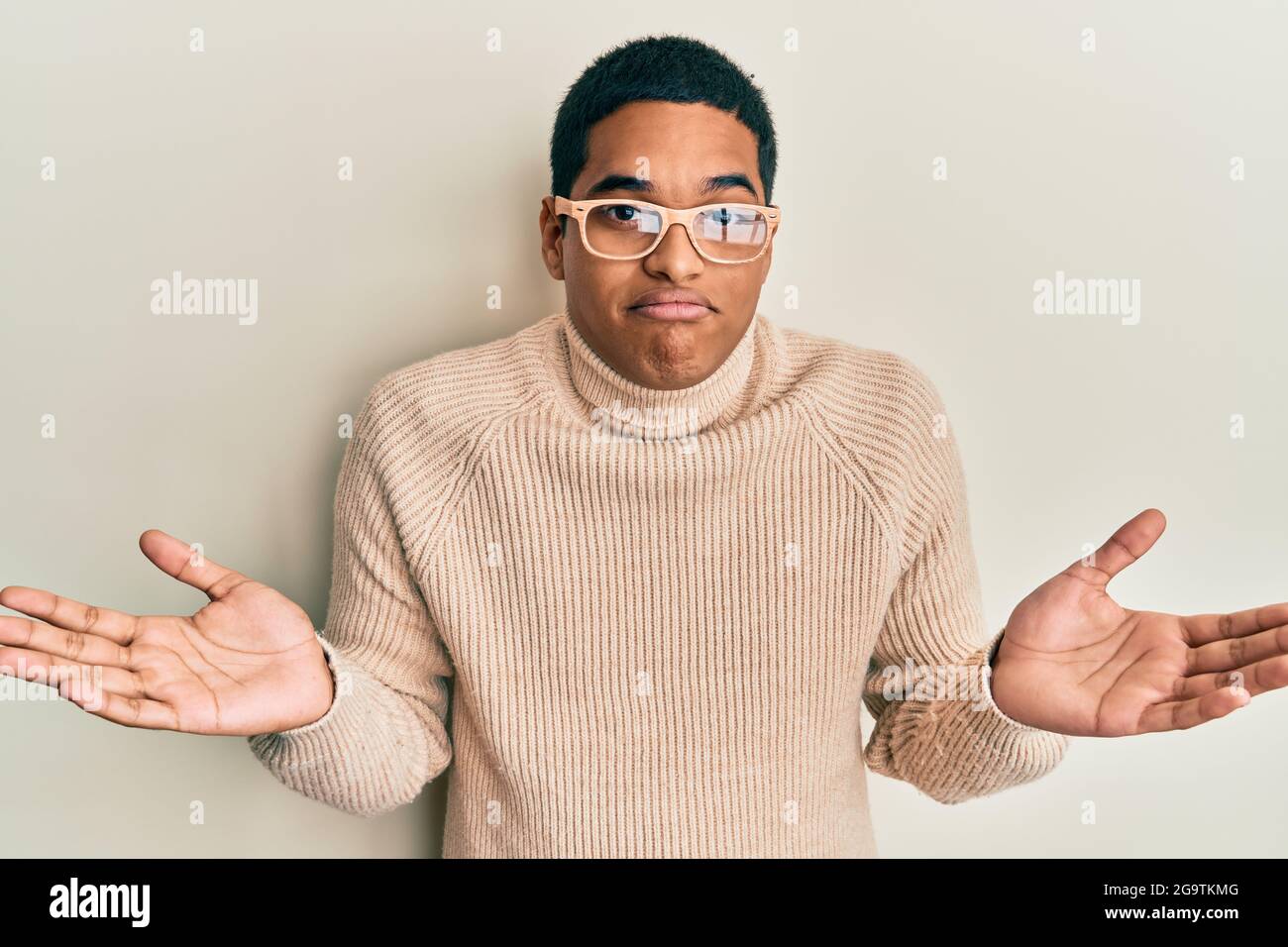 Young handsome hispanic man wearing turtleneck neck sweater and glasses  clueless and confused with open arms, no idea and doubtful face Stock Photo  - Alamy