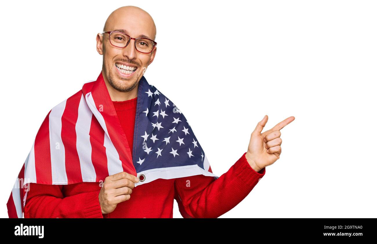 Bald man with beard wrapped around united states flag smiling happy pointing with hand and finger to the side Stock Photo