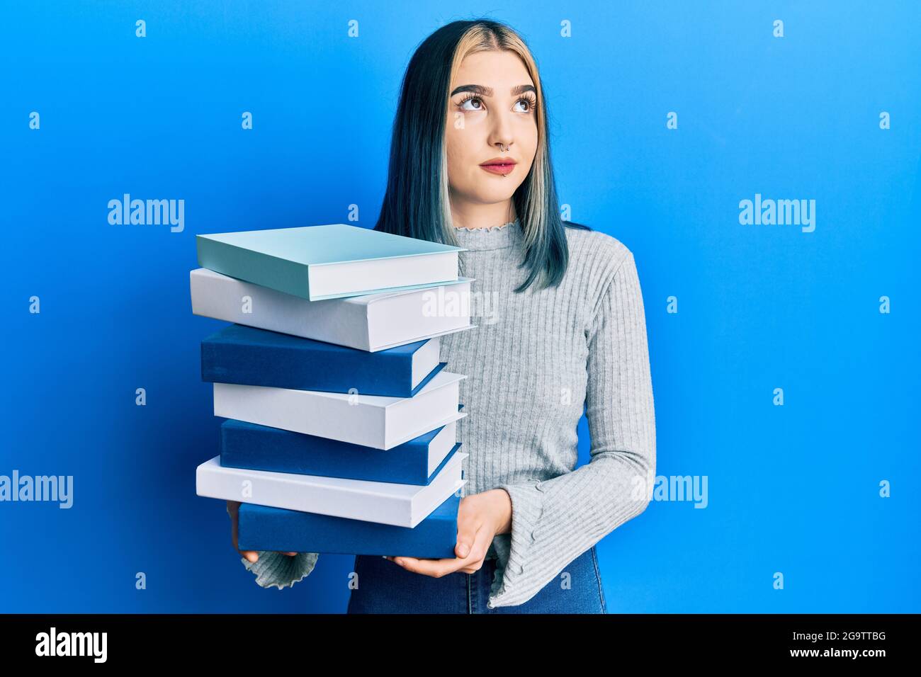 Young modern girl holding a pile of books smiling looking to the side ...