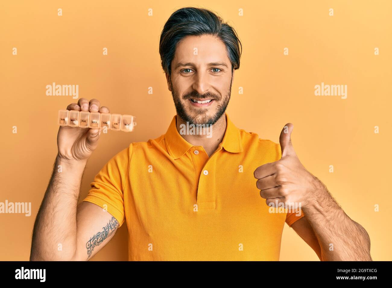 Young hispanic man holding pill organizer smiling happy and positive ...