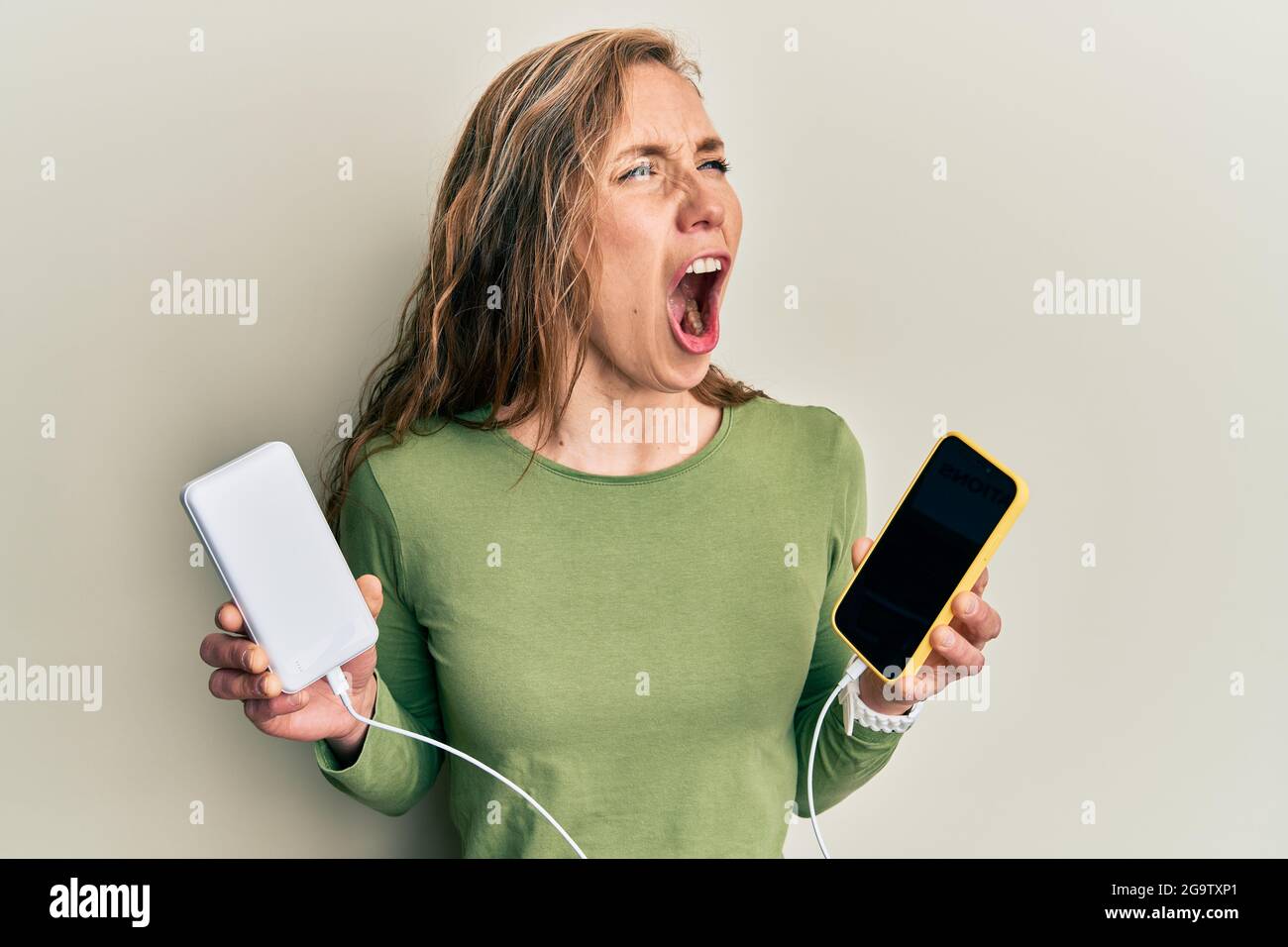 Young blonde woman charging smartphones angry and mad screaming ...