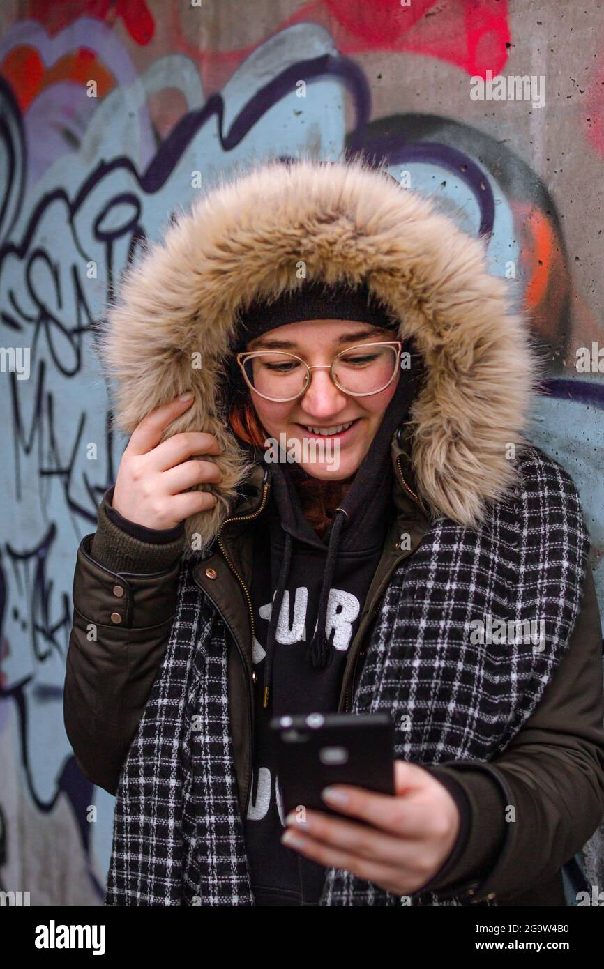 Lovely young woman receiving a video call on her mobile phone, practicing social distance and wearing a disposable face mask as protection Stock Photo