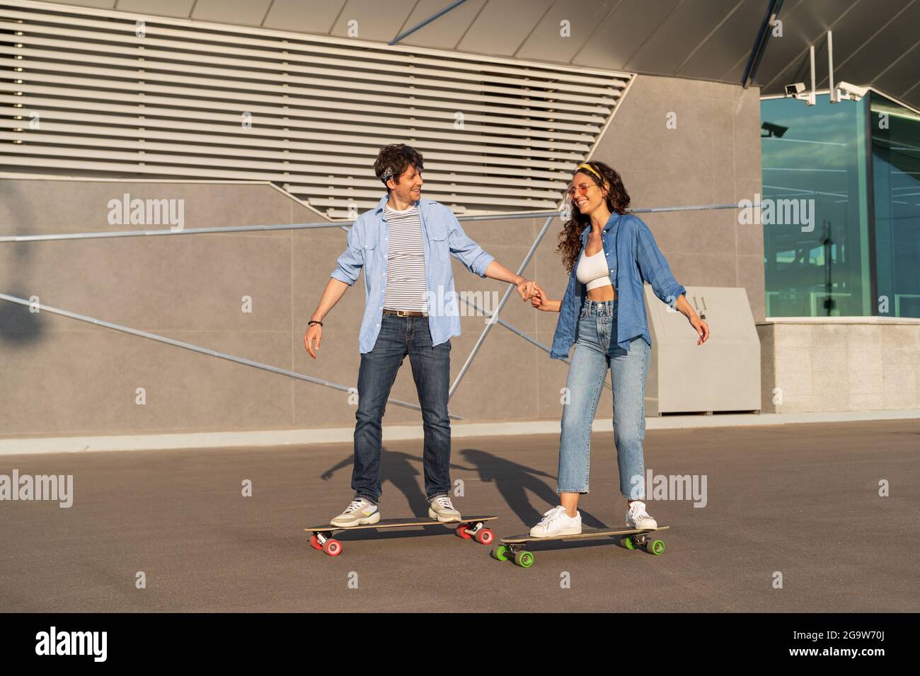 Trendy young couple skating on longboard together. Stylish man and woman longboarding in summer city Stock Photo