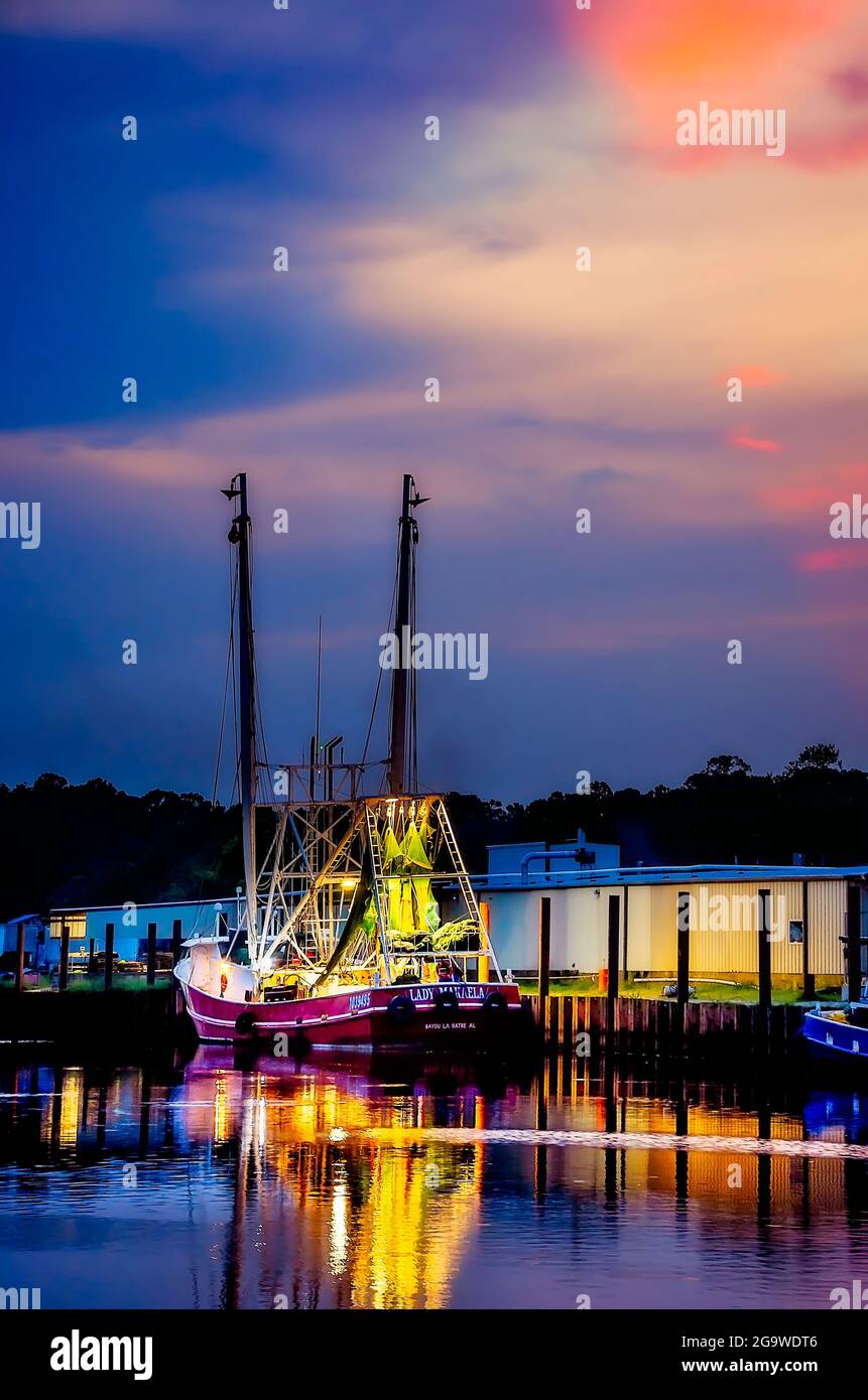 A shrimp boat is illuminated at dusk as the crew prepares to head out for a long night of shrimping, July 24, 2021, in Bayou La Batre, Alabama. Stock Photo