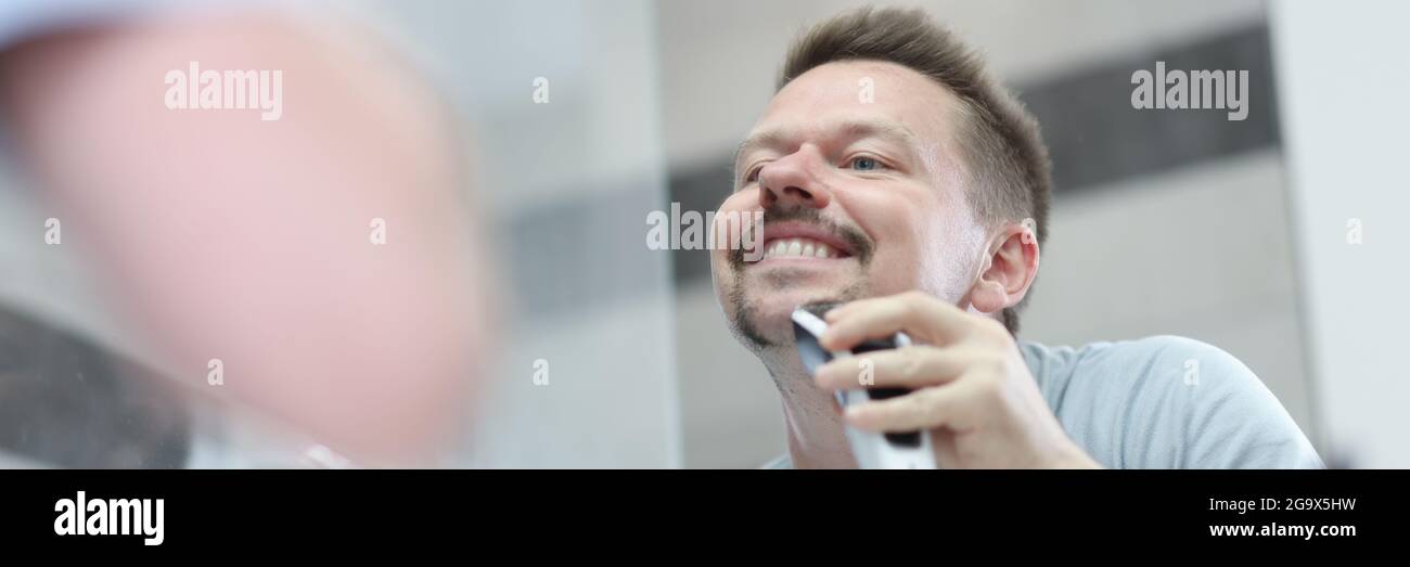Man shaves his stubble with machine in front of mirror Stock Photo