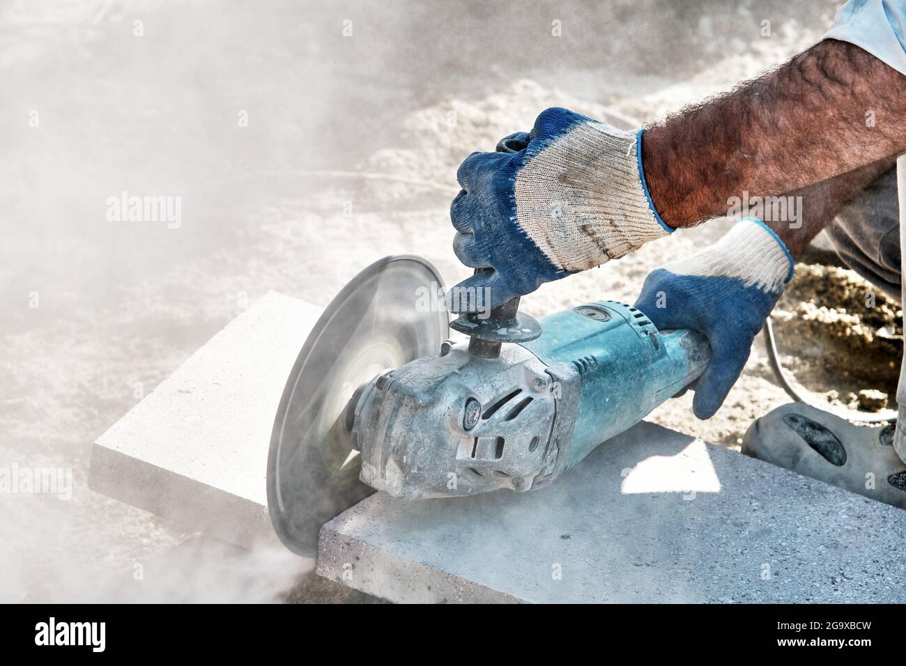 Hands of a pavement construction worker using an angle grinder for cutting the tiles. Stock Photo