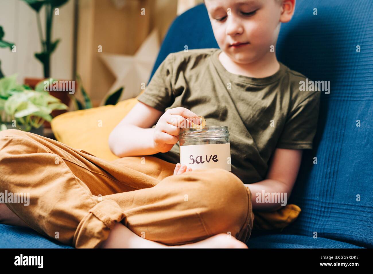 Close up of Little child kid boy hands grabbing and putting stack coins in to glass jar with save label. Donation, saving money, charity, family Stock Photo