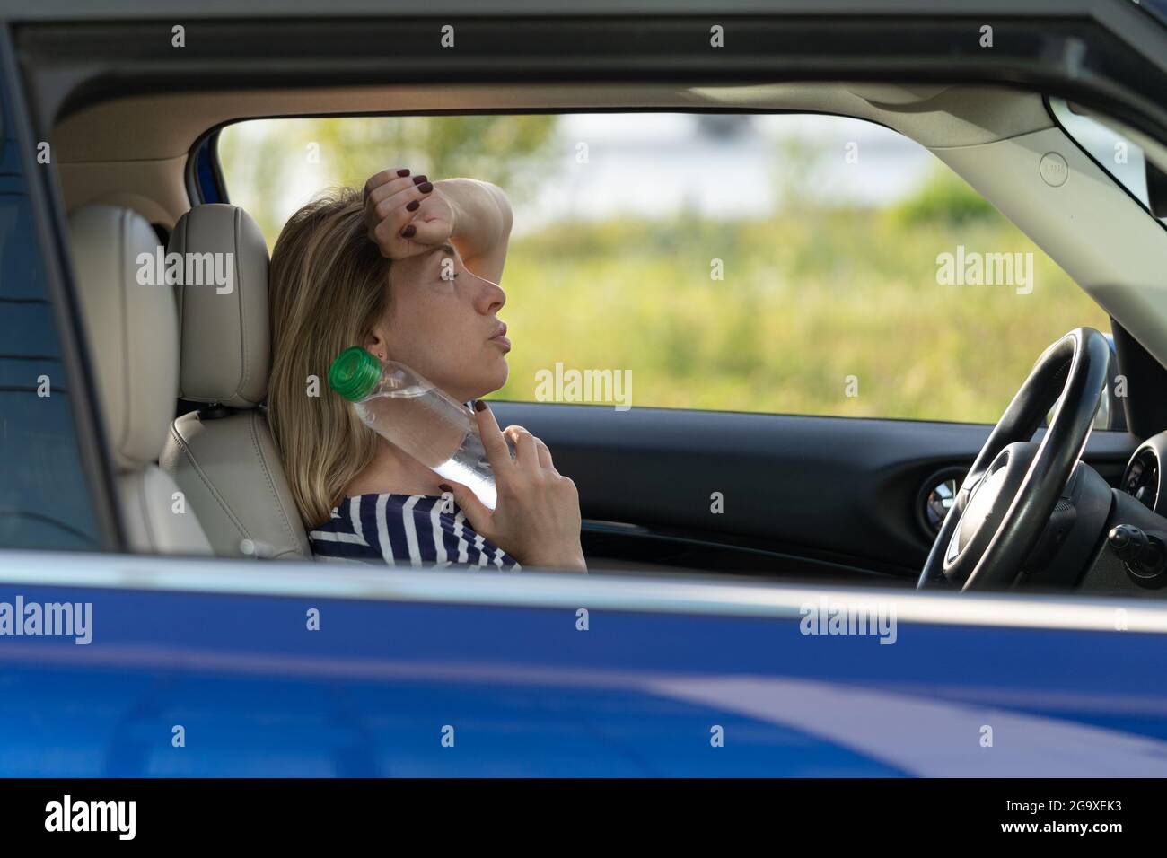 Exhausted girl driver suffering from headache, heat, hot weather applies bottle of water to neck Stock Photo