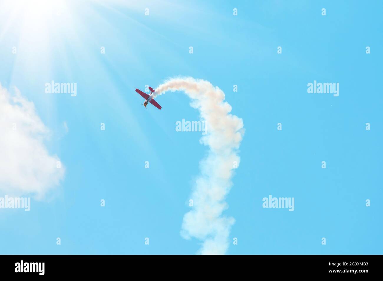 stunt plane trailing smoke bright sun and clouds Stock Photo