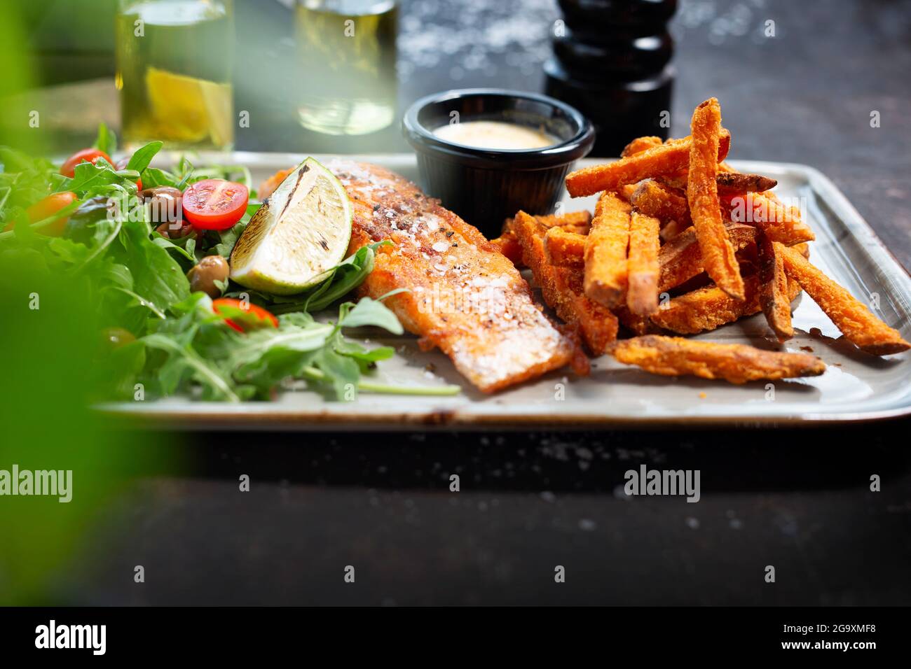 Grilled salmon with sweet potato fries, and salad. The cook cooks and serves an appetizing dish. The finished dish served on a plate. Serving proposal Stock Photo