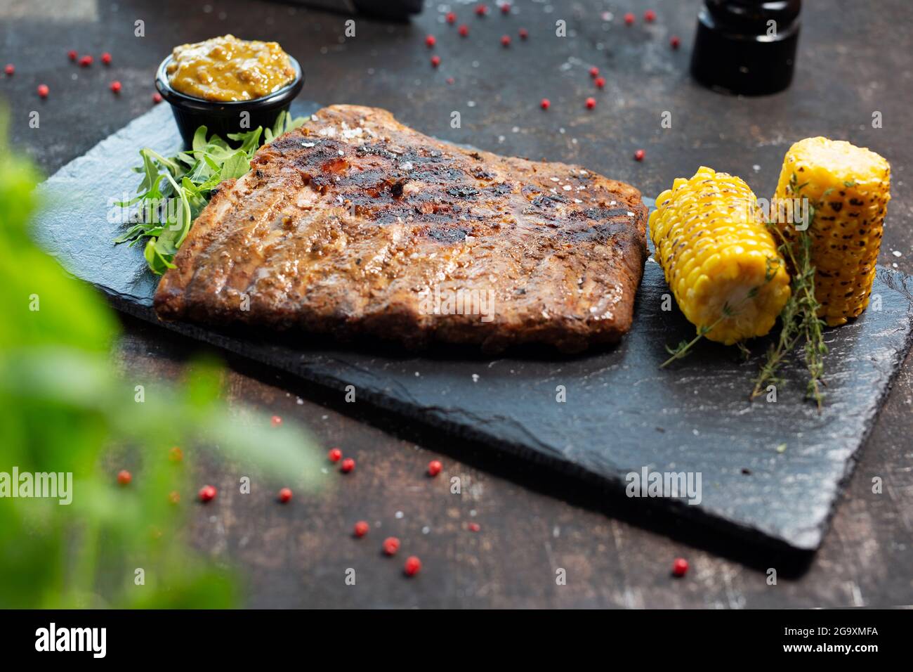 Grilled barbecue ribs, grilled corn cob, mustard sauce. The cook cooks and serves an appetizing dish. The finished dish served on a plate. Serving pro Stock Photo