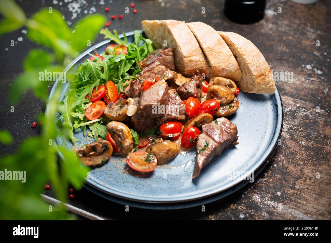 Liver stew with mushrooms and cherry tomatoes, served with bread and fresh salad. The cook cooks and serves an appetizing dish. The finished dish serv Stock Photo