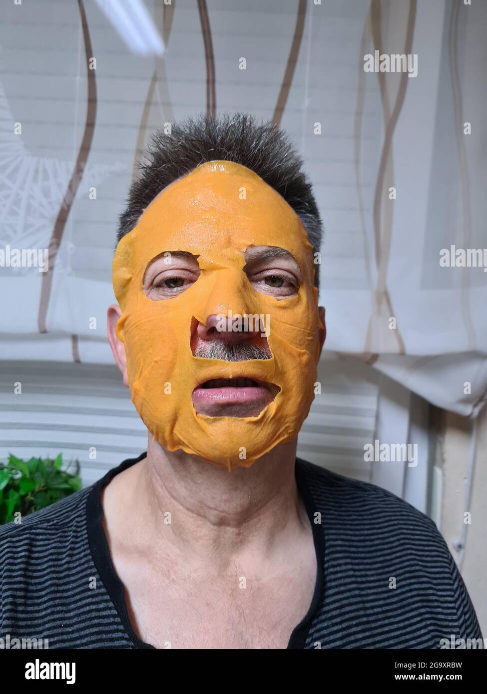 Young attractive and happy gay man in bathroom using beauty paper facial  mask touching his face looking to the mirror smiling in male beauty skin  care Stock Photo - Alamy