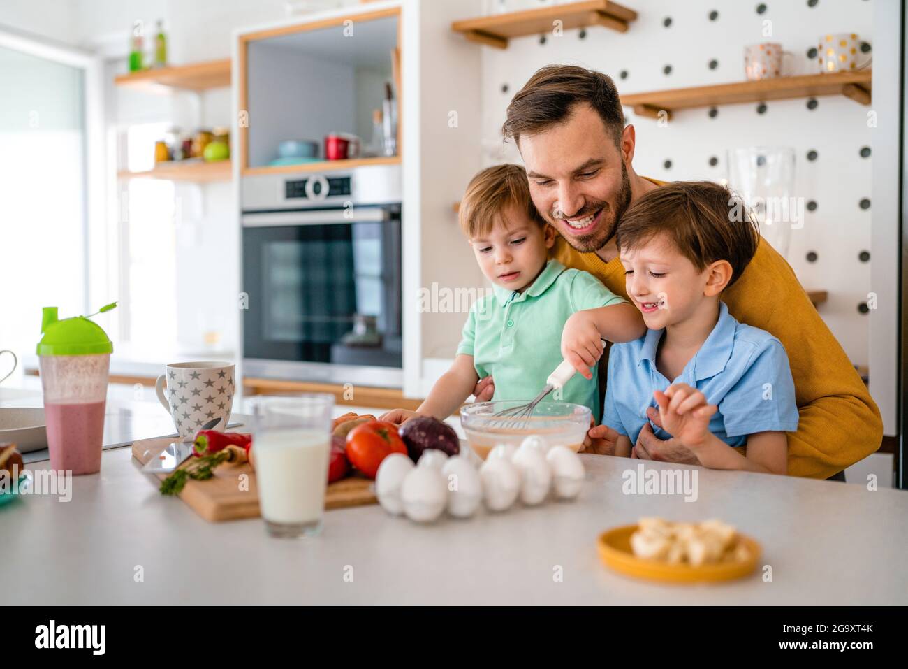 Happy single father with kids having fun and preparing healthy food in kitchen at home. Stock Photo