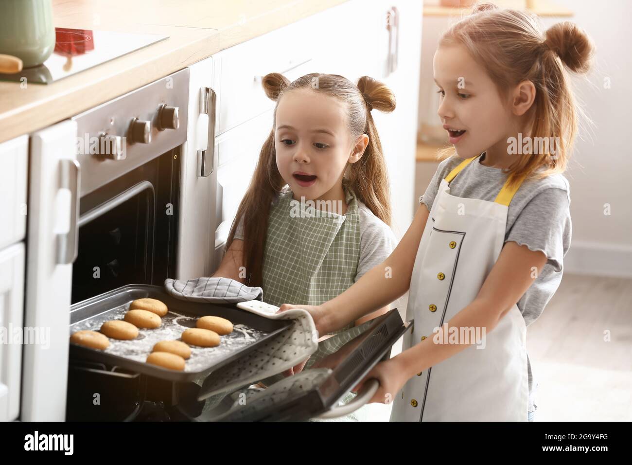 Cute little sisters taking tasty cookies from oven in kitchen Stock ...