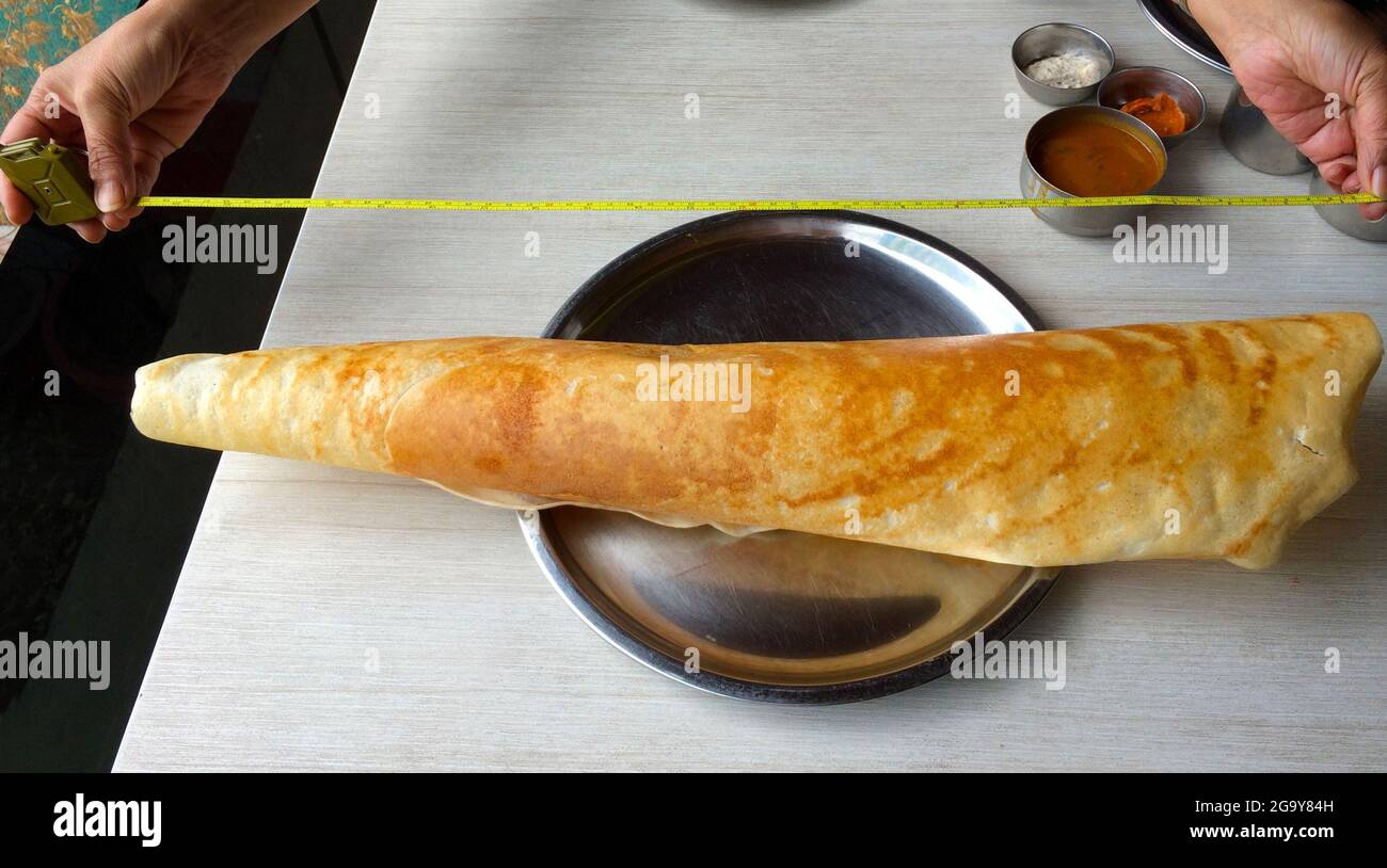 Person measuring an oversized dosa on a plate, India Stock Photo