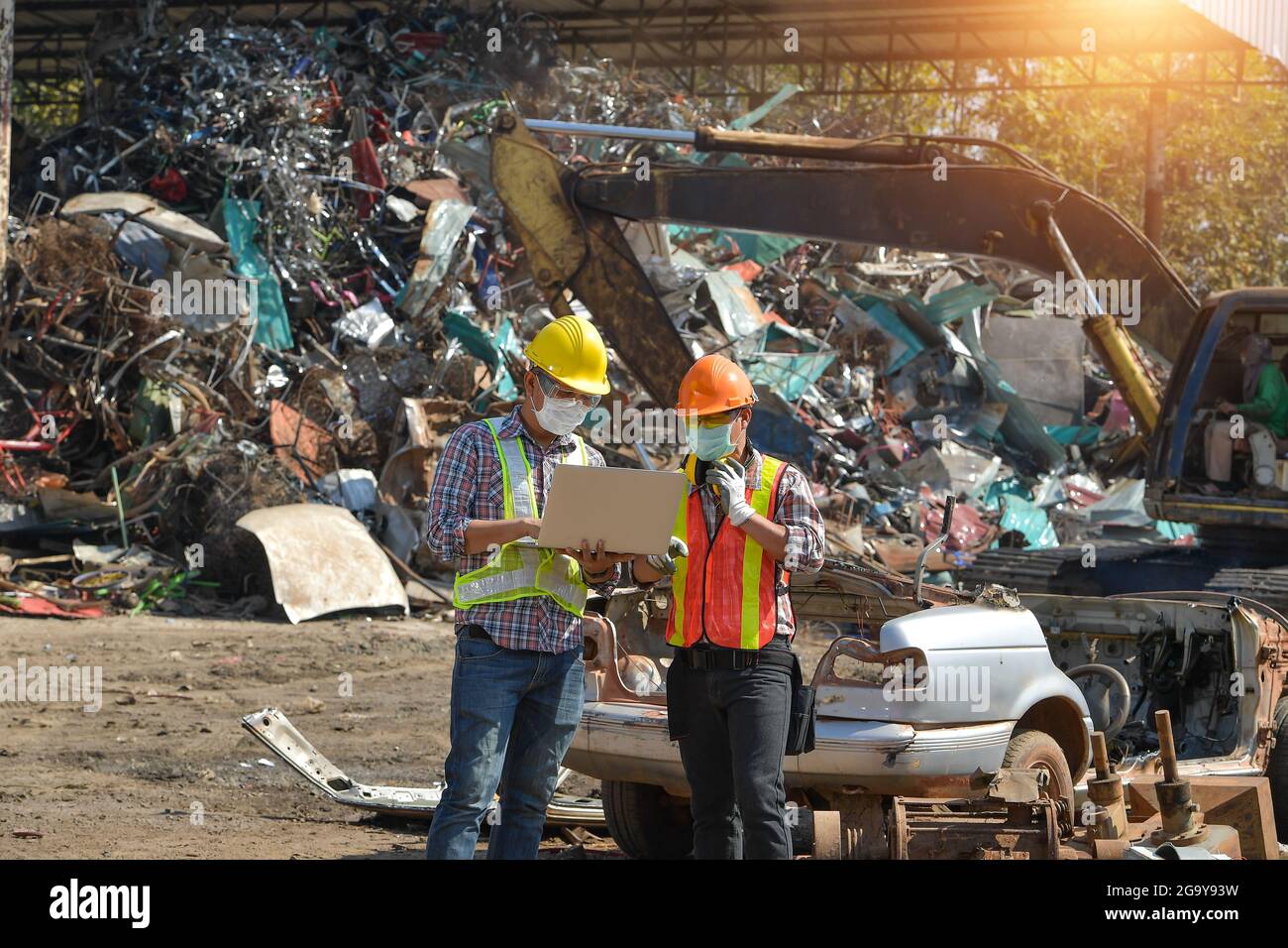 Two workers looking at a laptop at a scrap metal yard, Thailand Stock Photo