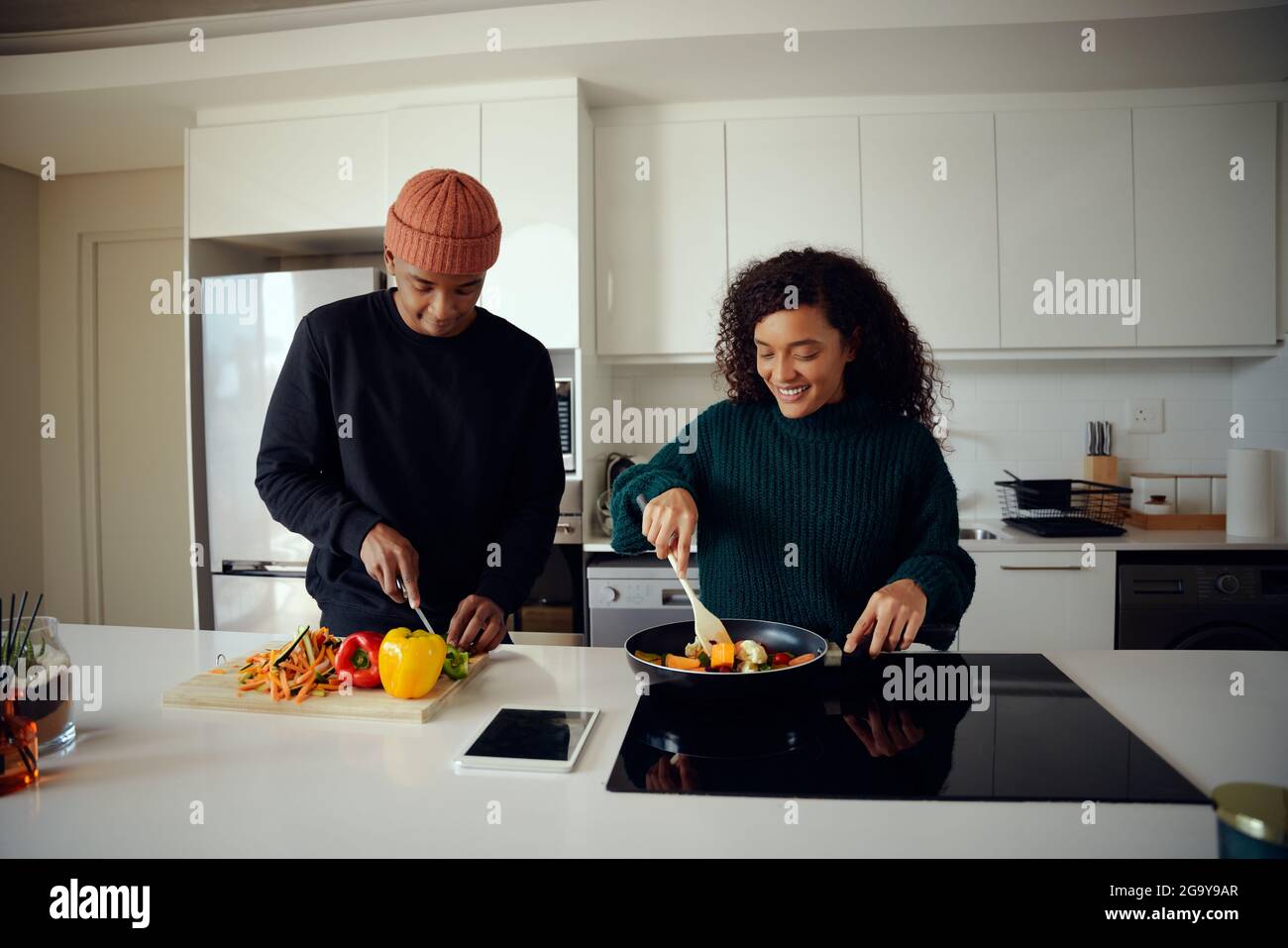 Young mixed race couple cooking food in the kitchen and using a tablet. Couple looking at tablet for food recipe. High quality photo Stock Photo