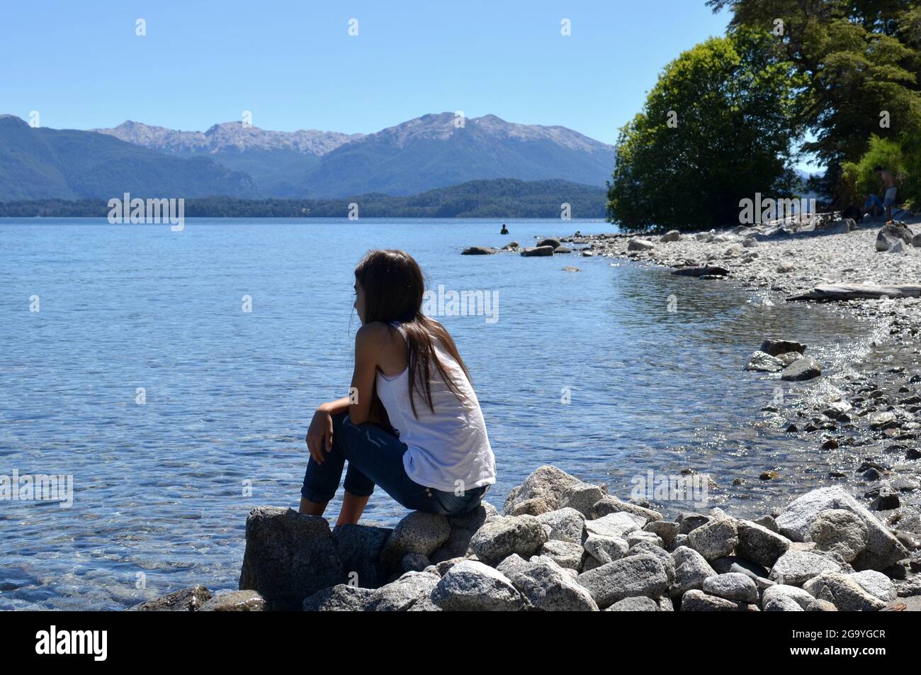 Girl sitting on rocks by Nahuel Huapi lake, Patagonia, Argentina Stock Photo