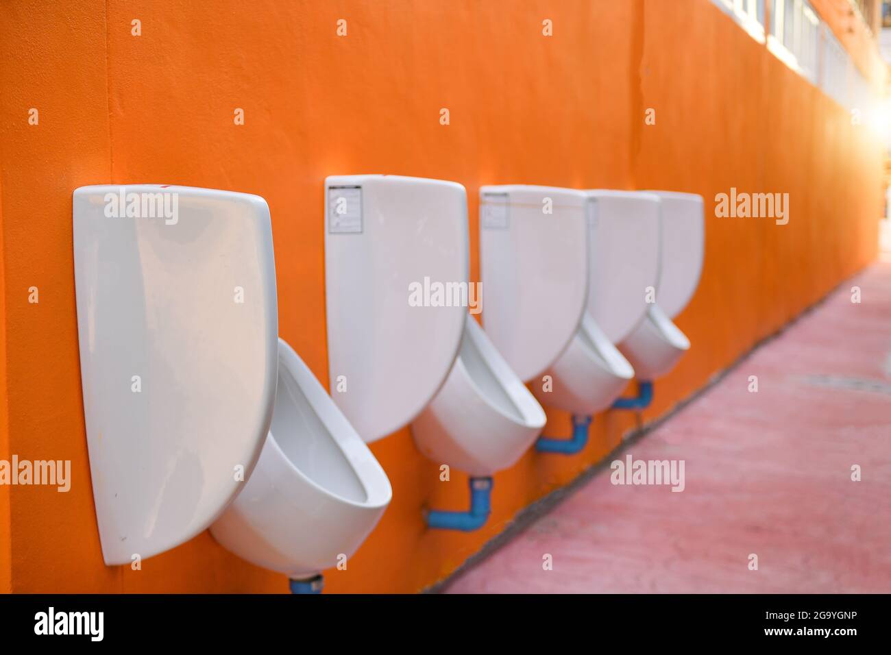 Row of Public urinals hanging on an orange wall Stock Photo