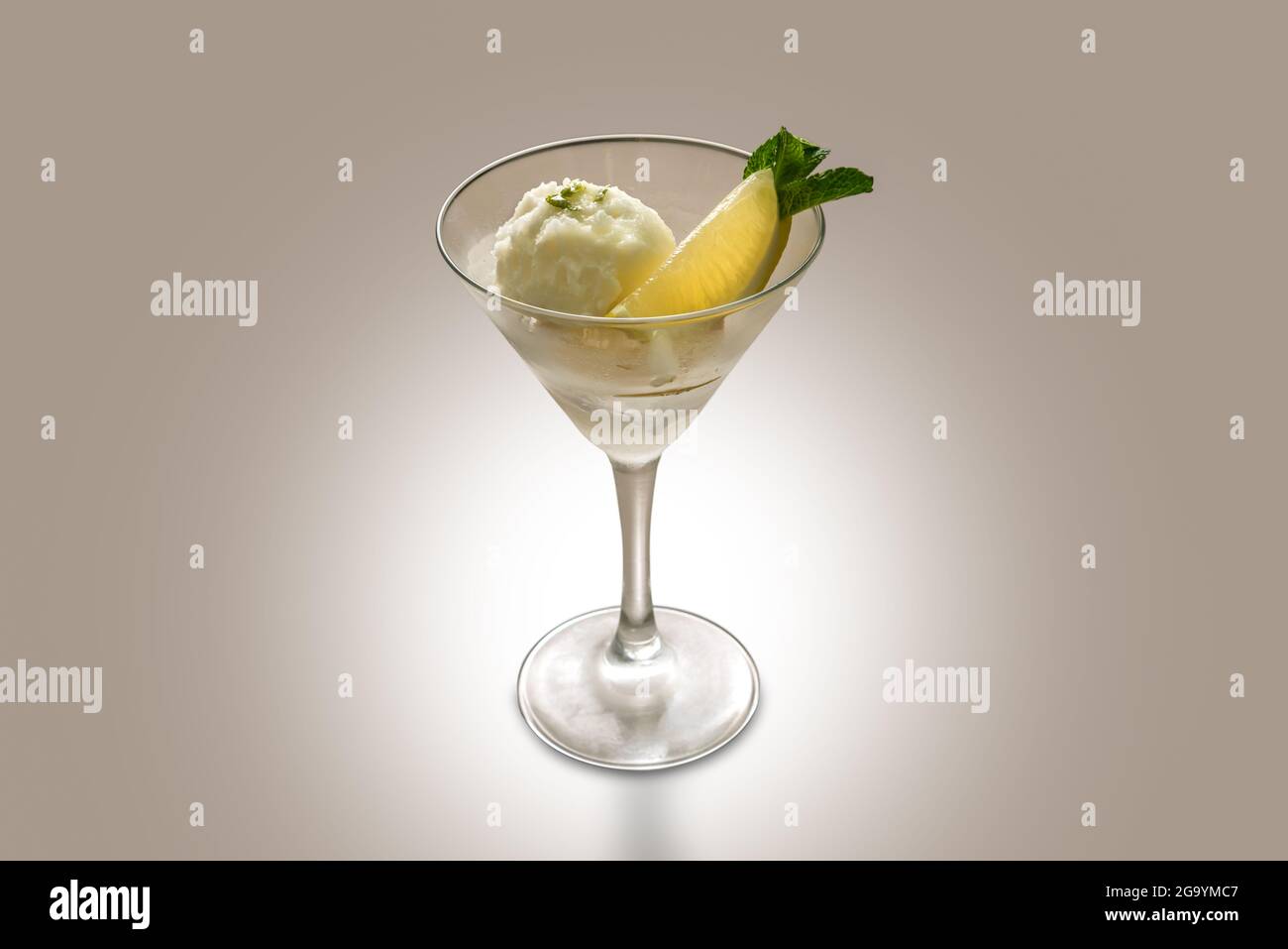 Lemon sorbet with lemon slice and mint leaves in martini glass on pale brown background, copy space Stock Photo