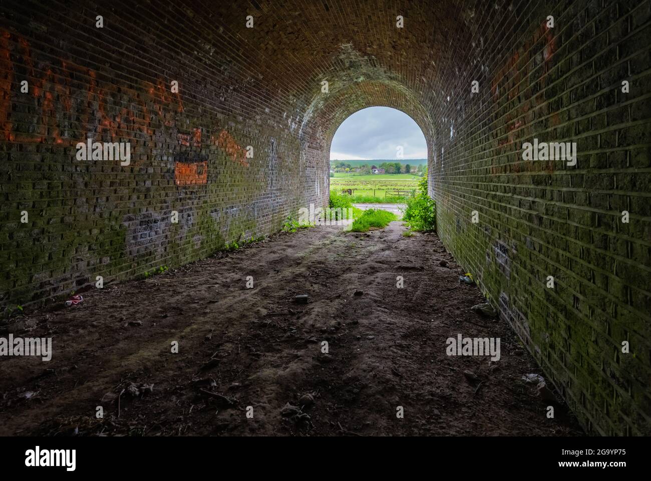 Inside a brick underline railway bridge, seemingly a tunnel, looking towards the exit using a wide angle lens in Amberley, West Sussex, England, UK. Stock Photo