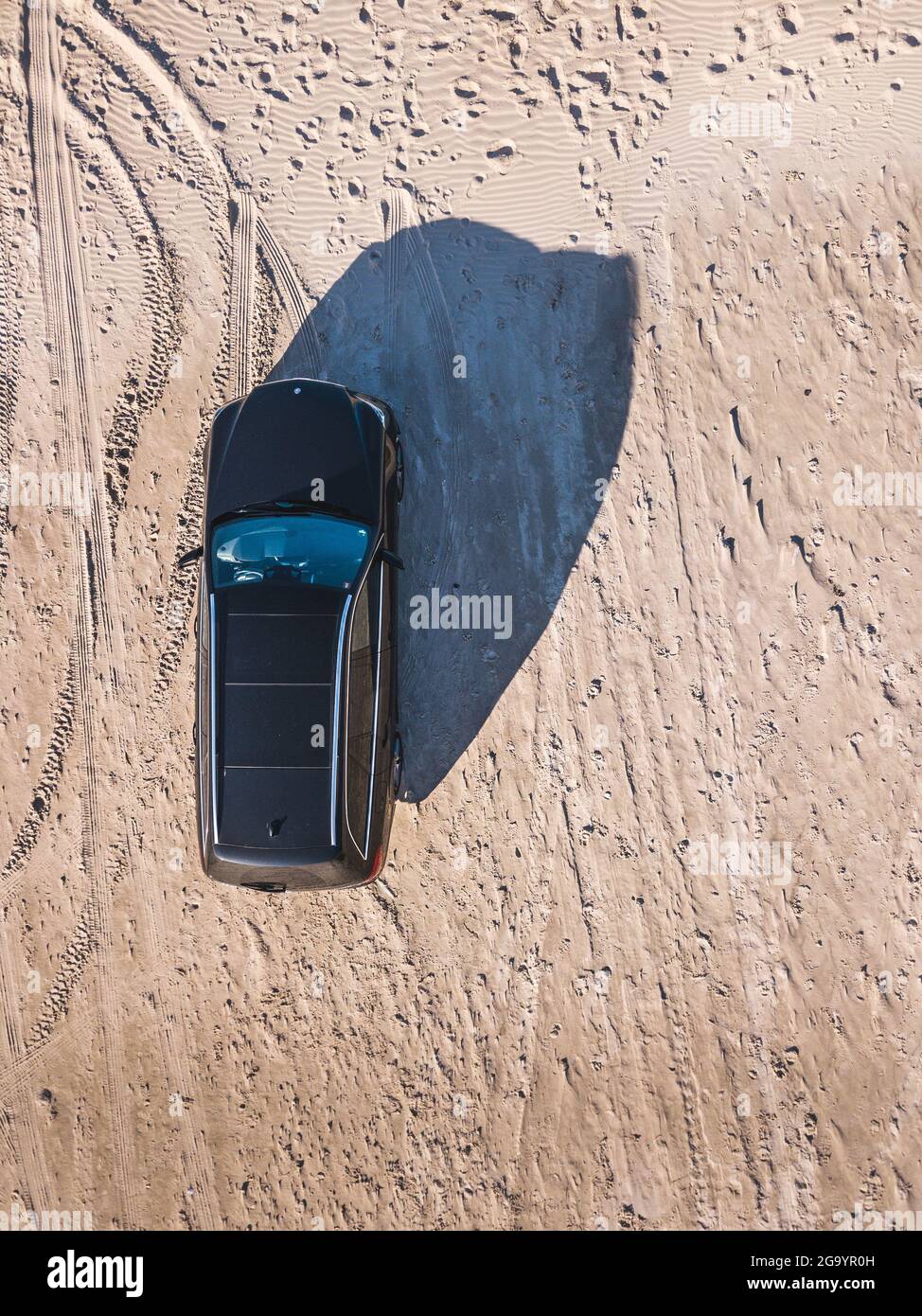 Black station wagon parked on a beach with tire tracks Stock Photo