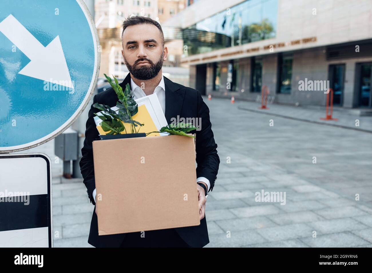 Depressed jobless person. Businessman standing with box of stuff outdoors near road sign, free space Stock Photo