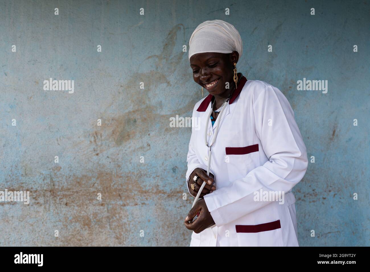 Beautiful smiling young Africanmedical intern with a stethoscope around her neck looking at the floor with a satisfied expression on her face after re Stock Photo