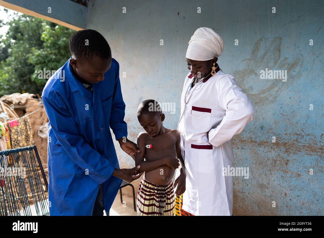 In this image, a young black medical assistenst is taking the temperature of a small toddler during a home visit, under the close supervision of a fem Stock Photo