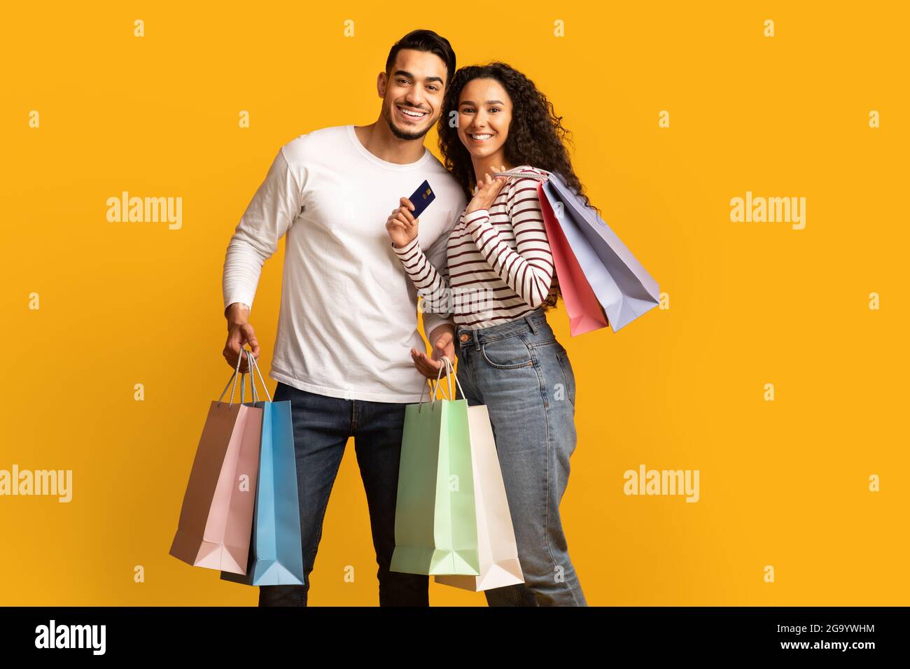 Cheerful Young Arab Couple Posing With Credit Card And Bright Shopping Bags Stock Photo