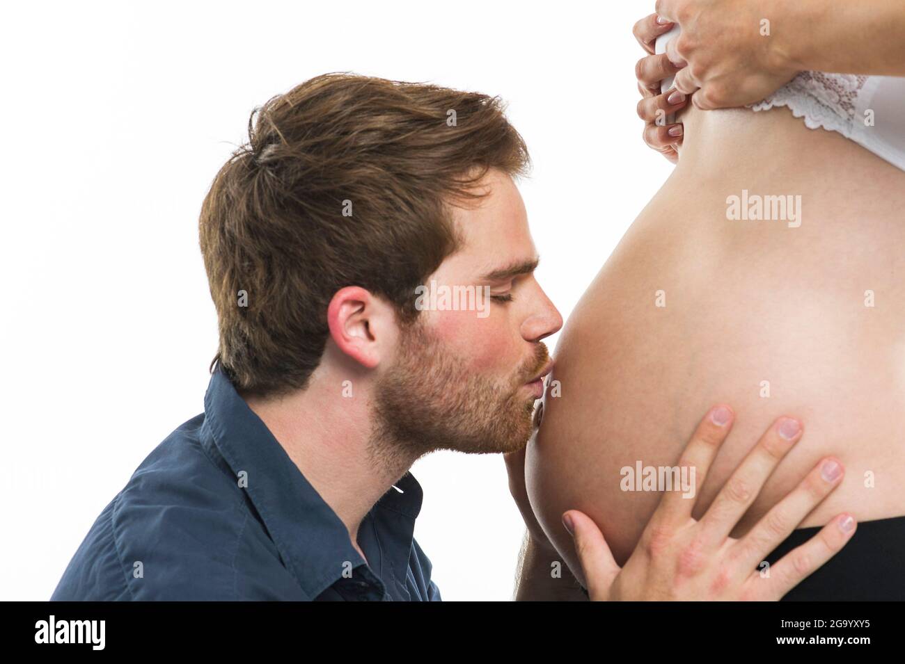 expectant father happily kissing his pregnant wife's baby bump, side view, Germany Stock Photo