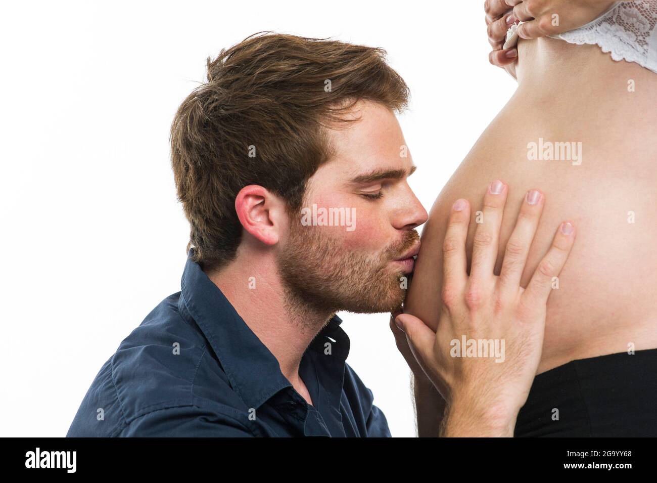 expectant father happily kissing his pregnant wife's baby bump, side view, Germany Stock Photo