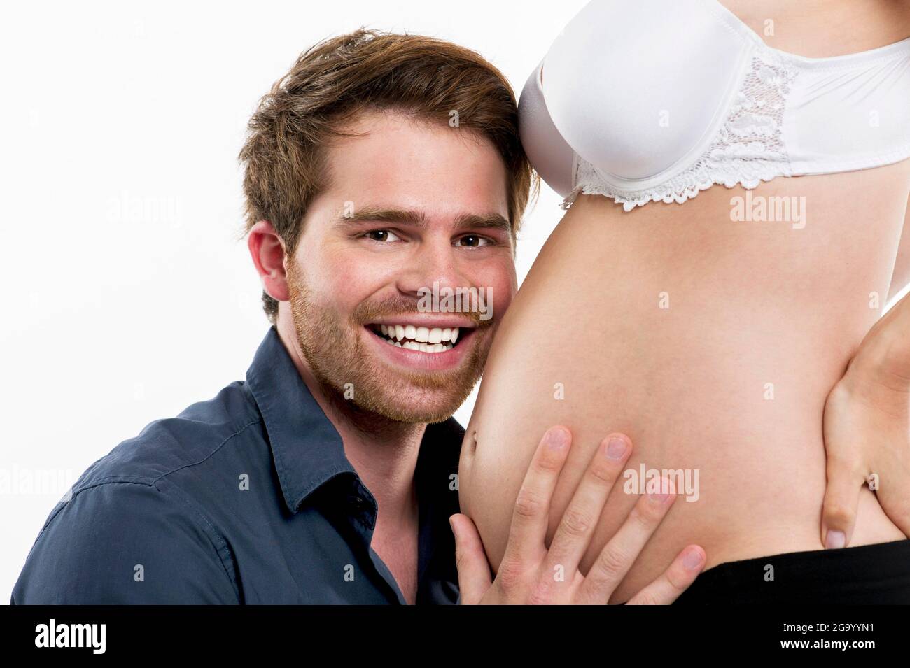 expectant father happily holding his pregnant wife's baby bump, side view, Germany Stock Photo