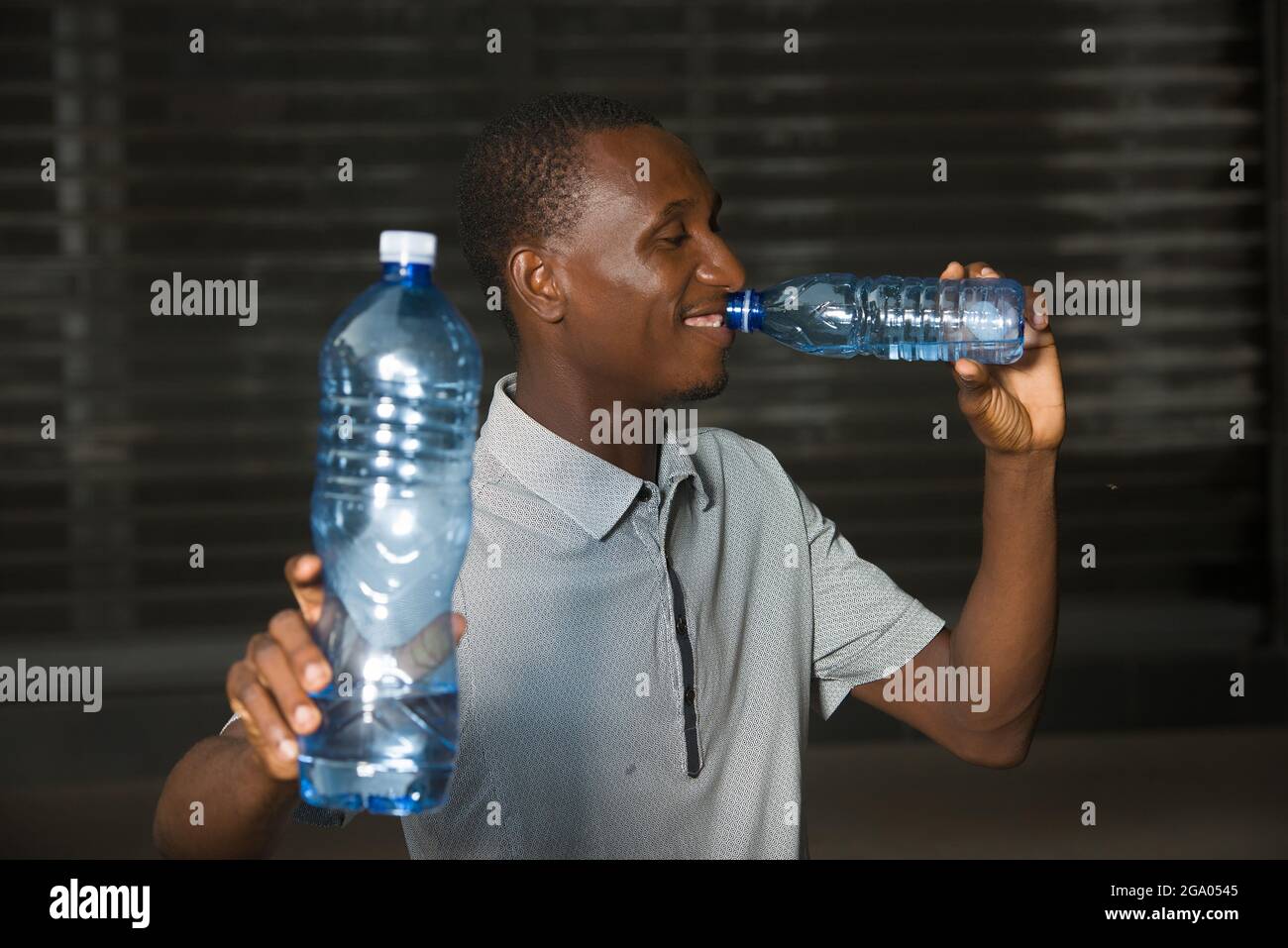 young man standing outdoors go drinking water while smiling. Stock Photo