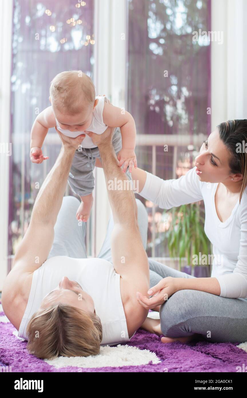Happy parents laying and sitting on the floor and playing with their baby boy. Father holding his child. Stock Photo