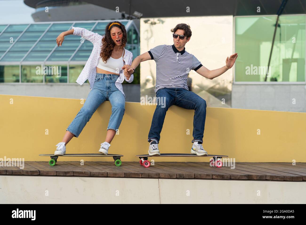 Young hipster couple have fun with longboard pretend ride skateboard sitting in urban skatepark Stock Photo