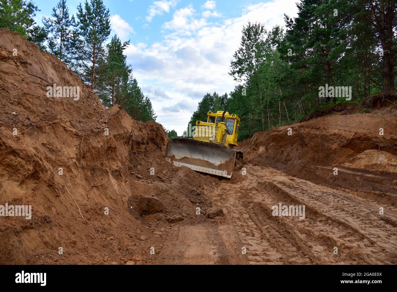 Dozer during clearing forest for construction new road . Yellow Bulldozer at forestry work Earth-moving equipment at road work, land clearing, grading Stock Photo