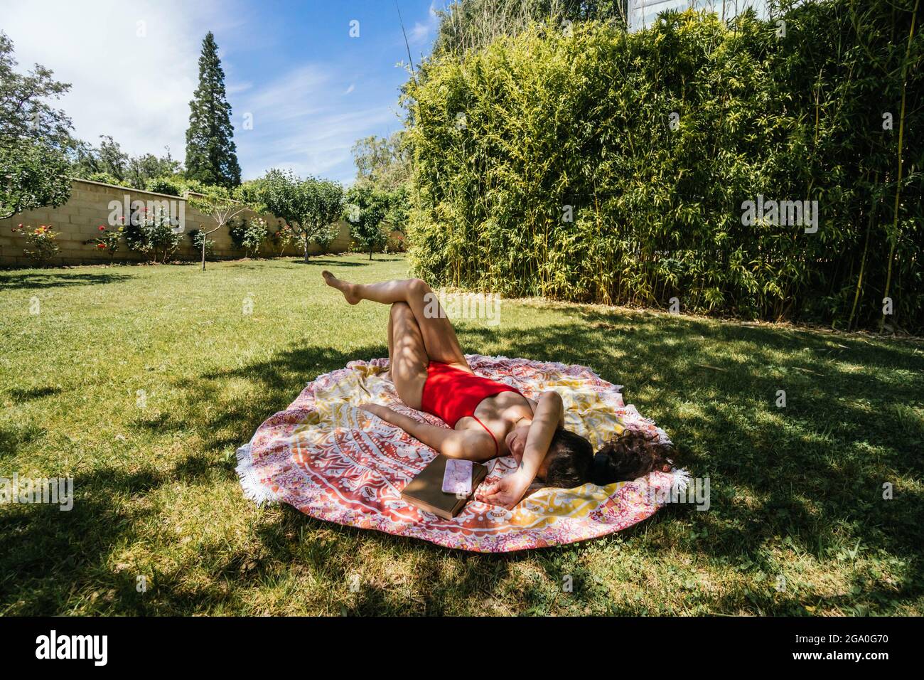 woman reading on a towel in the garden with swimsuit under a tree Stock Photo