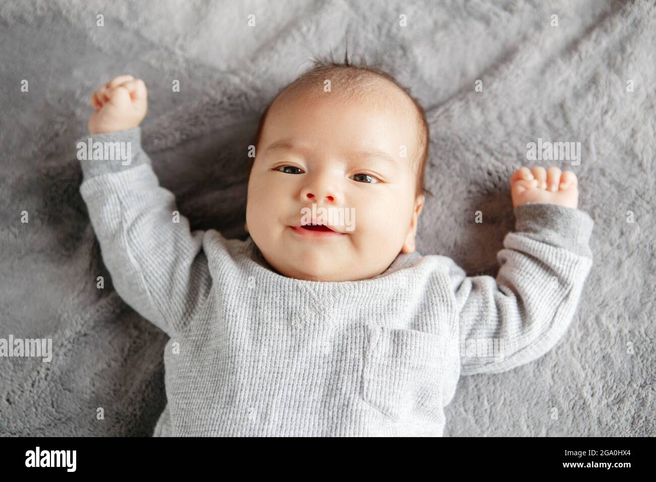 Cute little two months newborn Asian Chinese baby boy lying on his back. Alert awake aware baby boy looking at camera. View from high angle top above Stock Photo