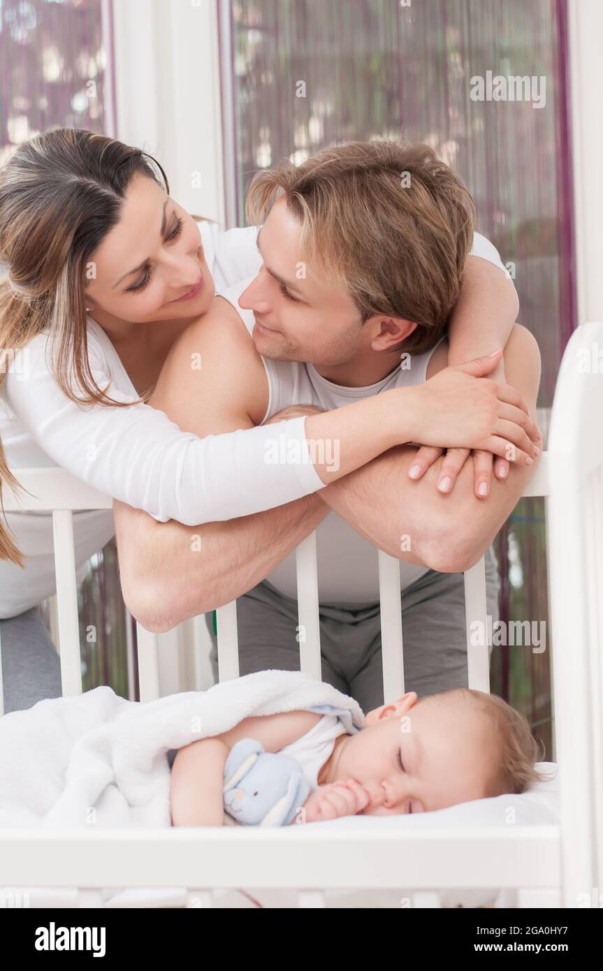 Happy parents standing beside the baby's bed. Happiness and pride. Stock Photo